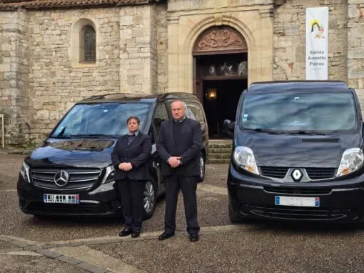 Agents funéraires posant devant deux corbillards noirs et une église en pierre
