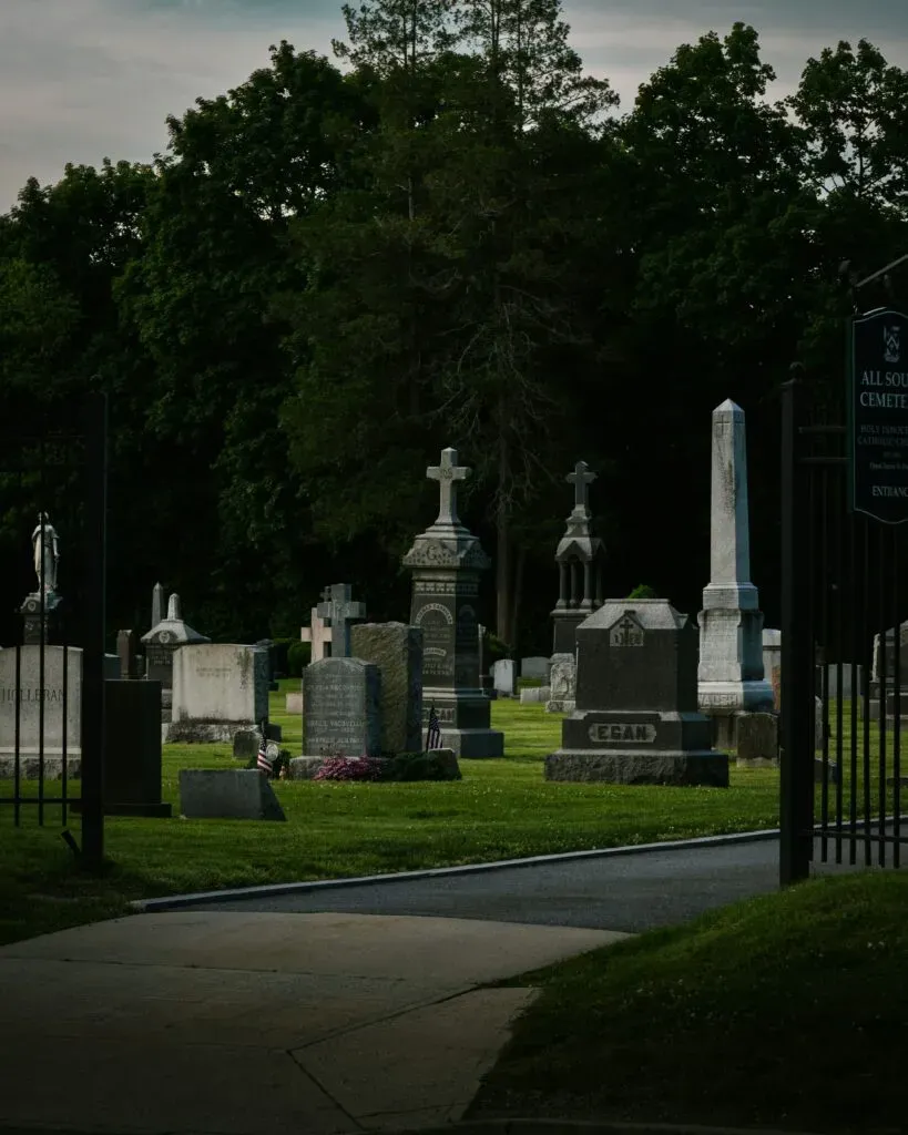 Allée d'un cimetière arboré bordée de monuments funéraires et croix