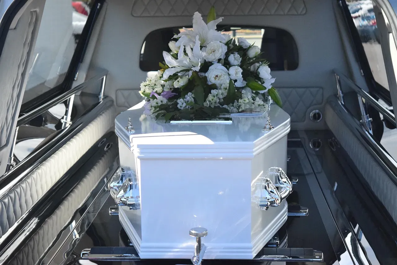 Cercueil blanc orné de fleurs blanches à l'intérieur d'un corbillard